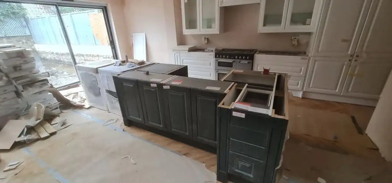 Dark shaker-style kitchen island being assembled in a London home extension with range cooker and white wall units in the background