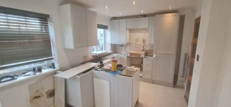 Grey shaker kitchen with peninsula unit mid-installation and tall larder units in a London home by ODS Plumbing & Construction