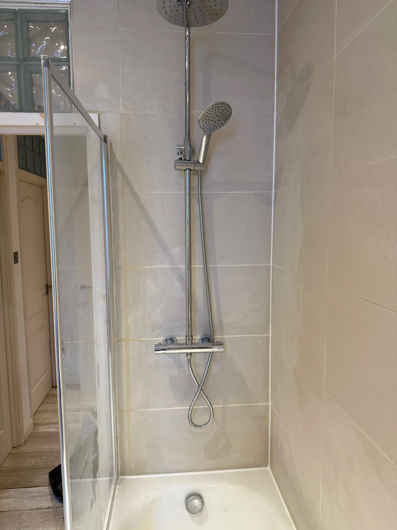 Chrome thermostatic shower column with rainfall head, hand shower and shower tray fitted in a cream tiled London bathroom by ODS Plumbing & Construction