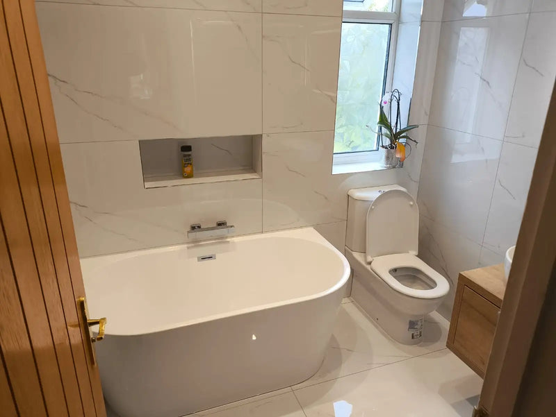 Modern bathroom with a white freestanding back-to-wall bath, marble-effect tiles, and recessed niche in London by ODS.