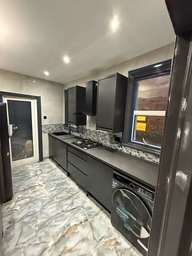 Graphite handleless kitchen with marble effect floor tiles, gas hob, integrated washing machine and mosaic splashback in London by ODS Plumbing & Construction
