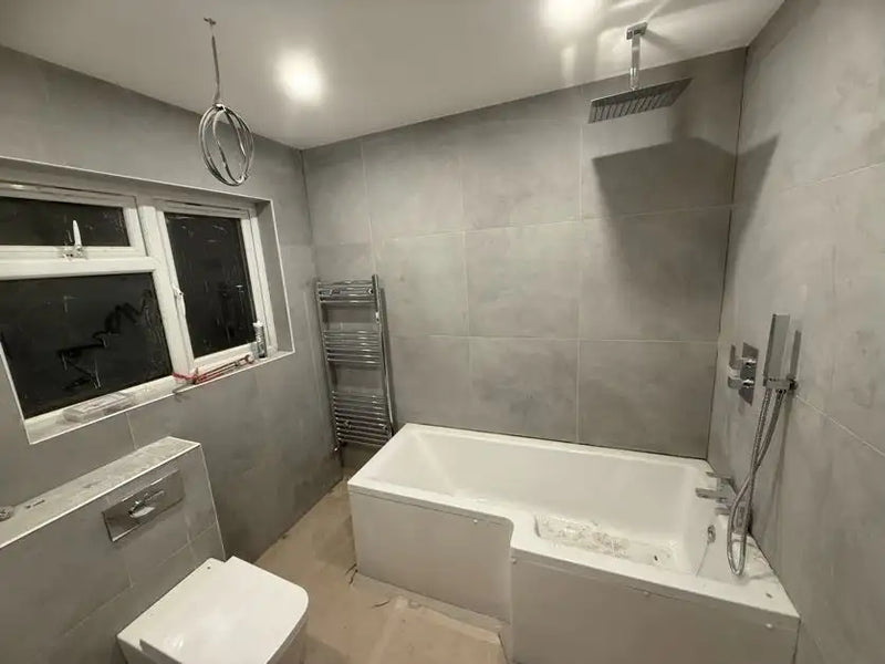 Grey large format concrete tile bathroom with freestanding bath, overhead ceiling shower and wall-hung toilet in London by ODS Plumbing & Construction