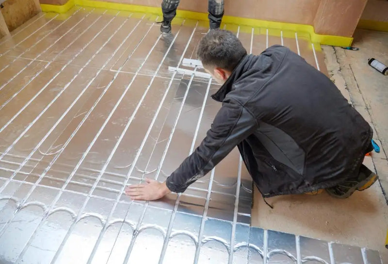 Engineer installing a low-profile wet underfloor heating system with reflective spread plates in a London residential property.