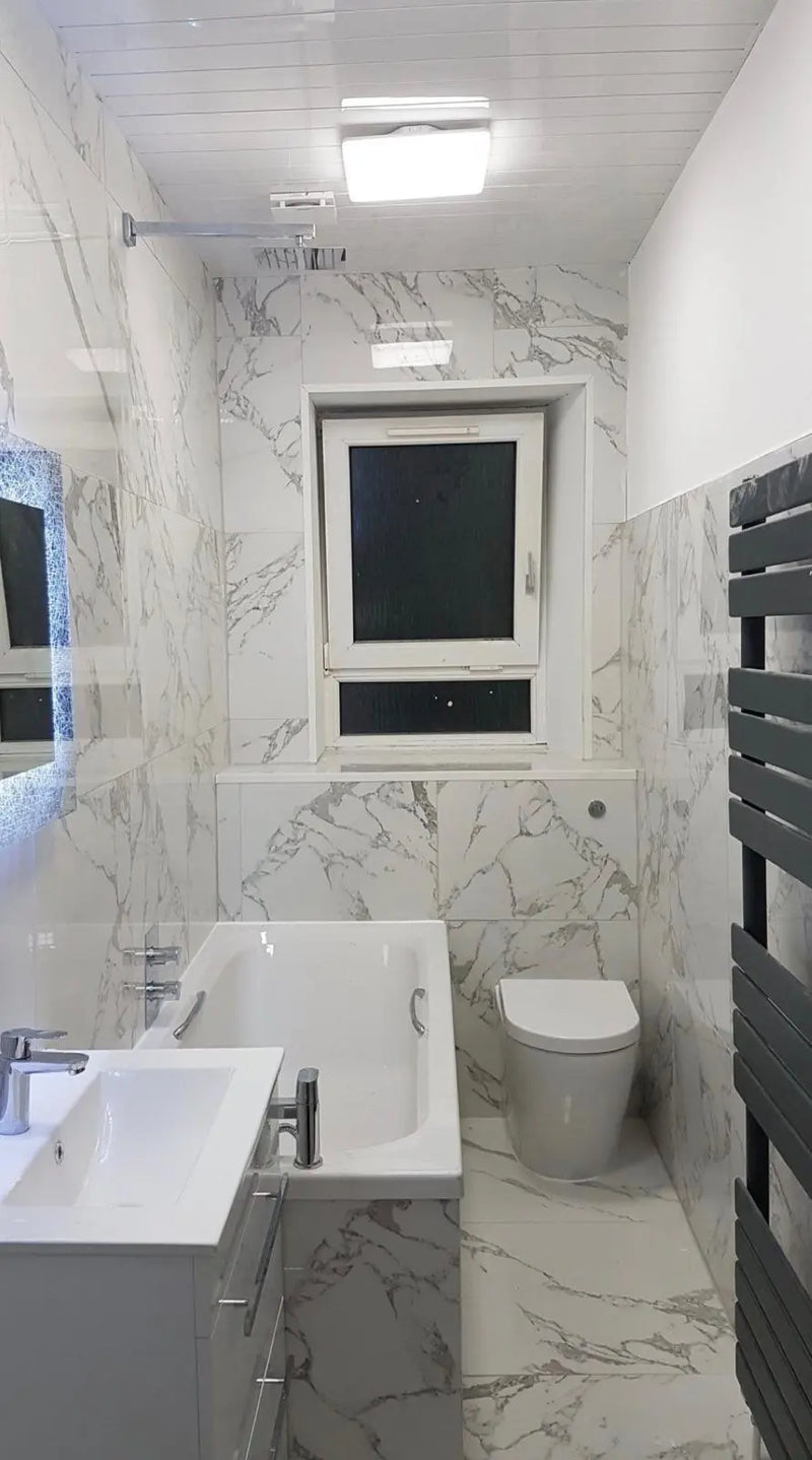 Luxury bathroom featuring marble-effect floor-to-ceiling tiling, a rainfall shower over a modern bath, and an anthracite towel radiator by ODS.