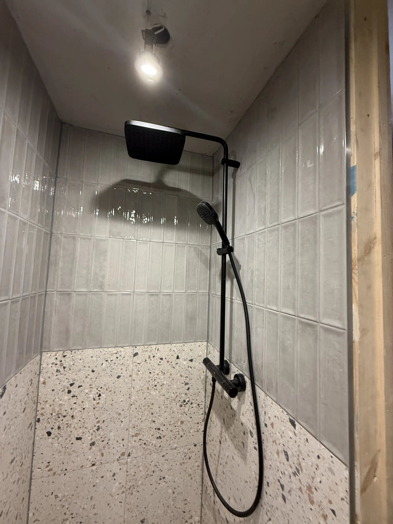 Matte black overhead shower system with hand shower and terrazzo lower tiles fitted in a London bathroom by ODS Plumbing & Construction