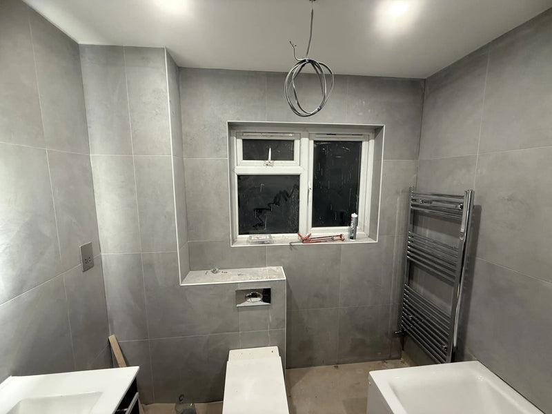 Modern bathroom renovation in London with grey large-format tiles, concealed cistern toilet, and chrome towel radiator.