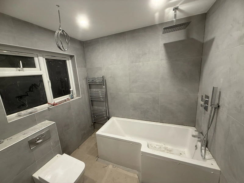 Modern bathroom renovation in London featuring grey large-format tiles, an L-shaped shower bath, and rainfall showerhead by ODS.