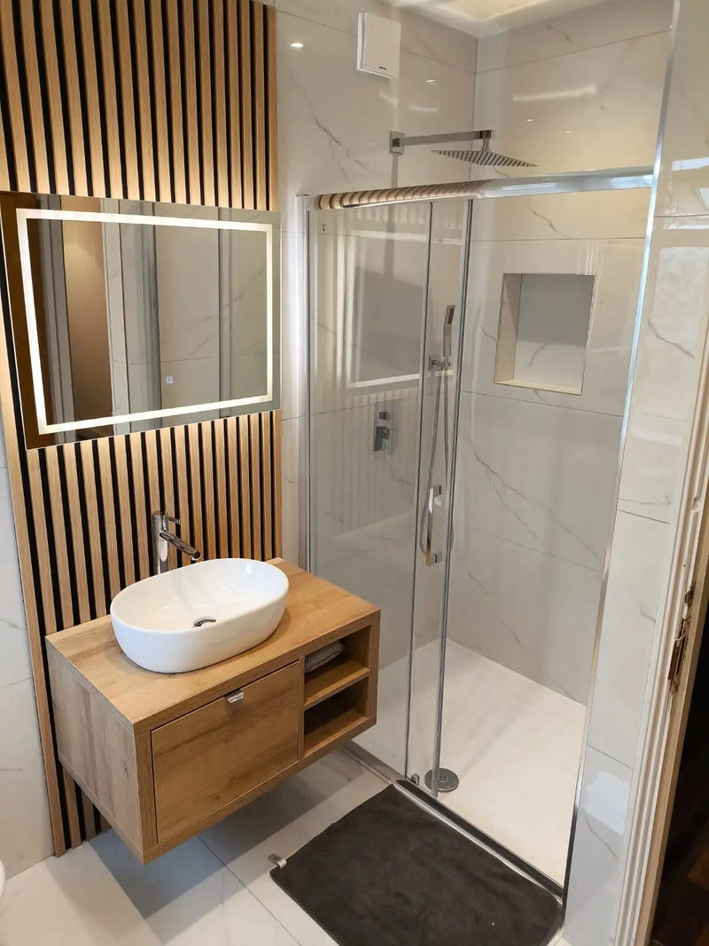 Luxury bathroom with oak slat wall, LED mirror, vessel sink, and marble-effect shower in London by ODS Construction.