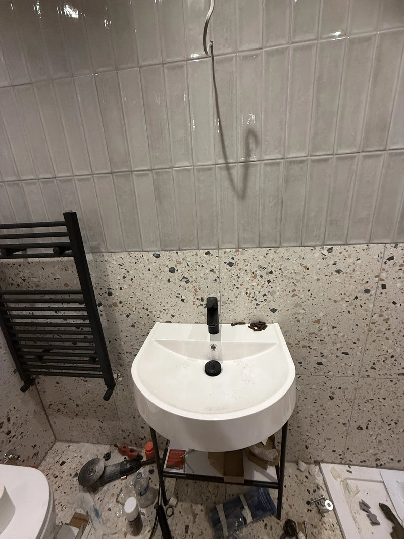 White semi-recessed basin on black metal stand with matte black tap and terrazzo wall tiles being fitted in a London cloakroom by ODS Plumbing & Construction