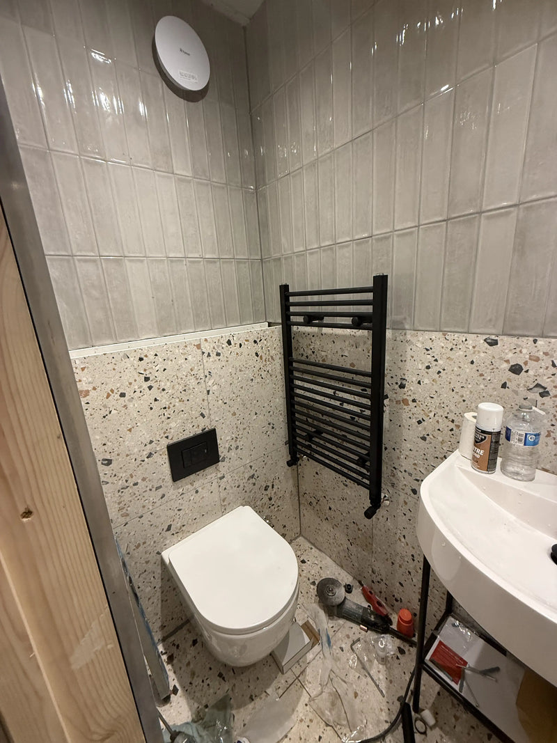 Terrazzo tiled cloakroom with wall-hung toilet, black heated towel rail and white metro tiles being fitted in London by ODS Plumbing & Construction