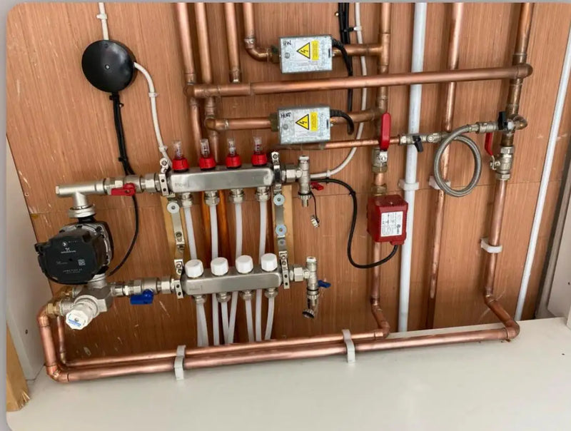 Technical installation of an underfloor heating manifold with flow meters, zone valves, and circulation pump by ODS Plumbing & Construction.