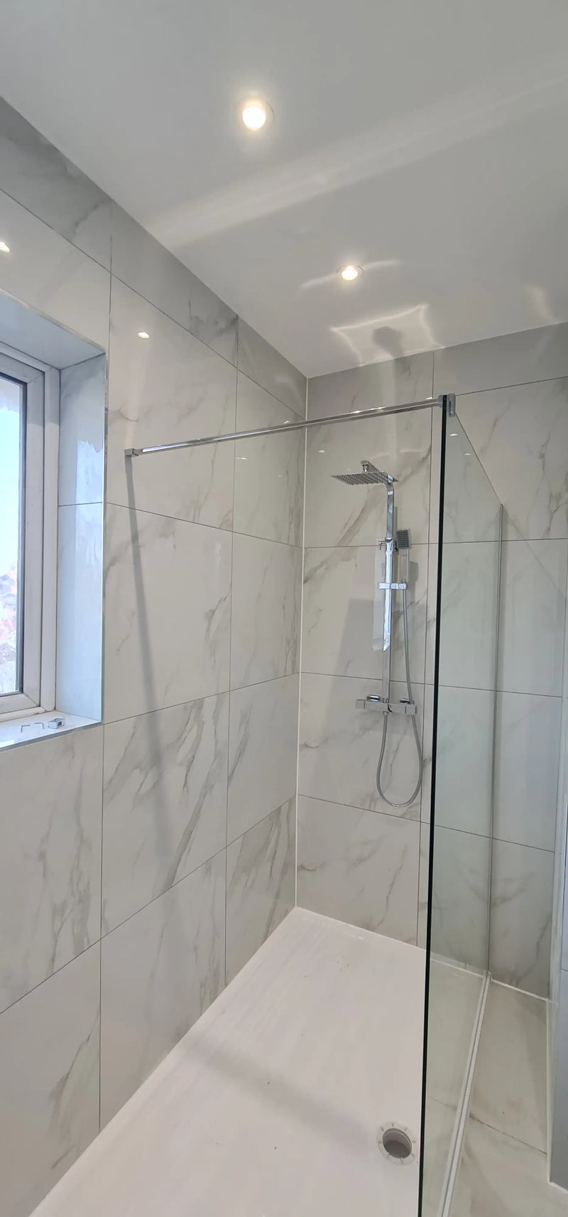 Luxury walk-in shower with marble-effect tiles, glass screen, and rainfall showerhead in London by ODS Construction.