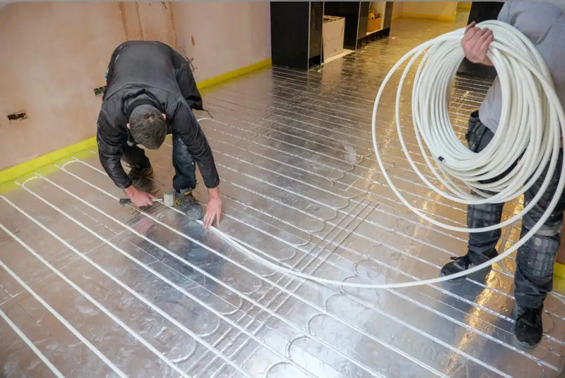 ODS Plumbing & Construction engineers installing white UFH piping onto reflective insulation panels in a London home.