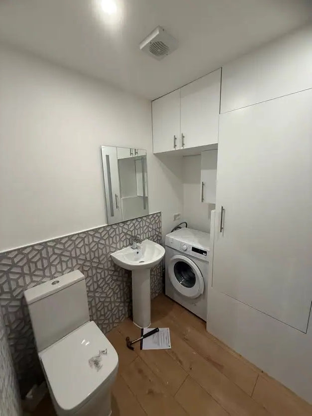 White bathroom with integrated washing machine, geometric floor tiles, wall-hung toilet and vanity unit fitted in London by ODS Plumbing & Construction