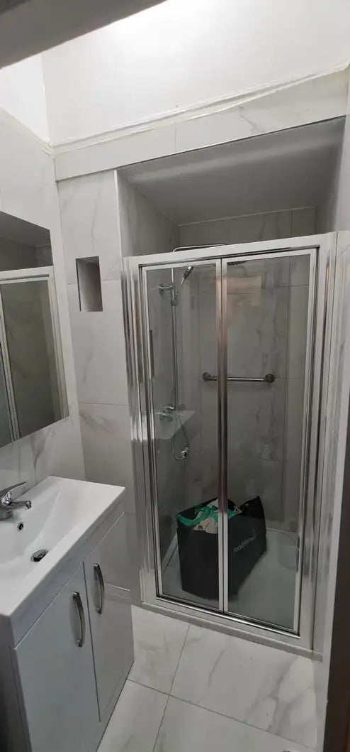 White marble effect tiled bathroom with chrome shower enclosure, vanity unit and basin newly fitted in London by ODS Plumbing & Construction
